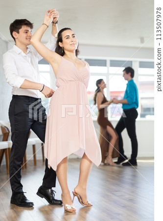 Girl and guy enjoying passionate latin american dancing with male partner in dance hall Girl and guy enjoying passionate latin american dancing with male partner in dance hall 113507978