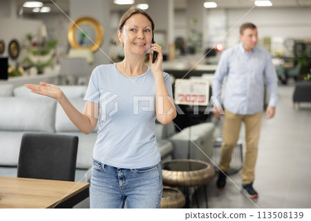Cheerful woman talking on mobile phone while strolling through furniture store Cheerful woman talking on mobile phone while strolling through furniture store 113508139