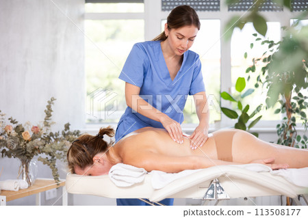 Young female massage therapist doing back massage to woman Young female massage therapist doing back massage to woman 113508177