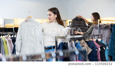 Young female consumer choosing windbreaker jackets in shopping center Young female consumer choosing windbreaker jackets in shopping center 113508232