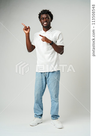 Young African Man Pointing at Something Against Gray Background Young African Man Pointing at Something Against Gray Background 113508548