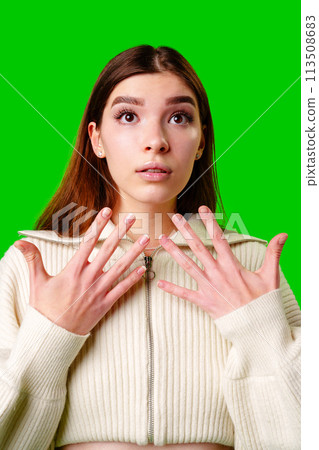 Young Woman With a Surprised Expression Standing Against a Green Background in Daylight 113508683
