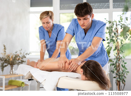 Two female and male masseuses perform stroking and rubbing of muscles of back and shoulders to girl Two female and male masseuses perform stroking and rubbing of muscles of back and shoulders to girl 113508977