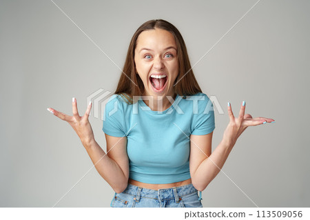 Happy cute young beautiful woman looking excited and surprised on gray background Happy cute young beautiful woman looking excited and surprised on gray background 113509056