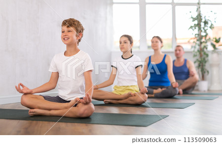 Happy preteen boy practicing lotus pose of yoga with his family Happy preteen boy practicing lotus pose of yoga with his family 113509063