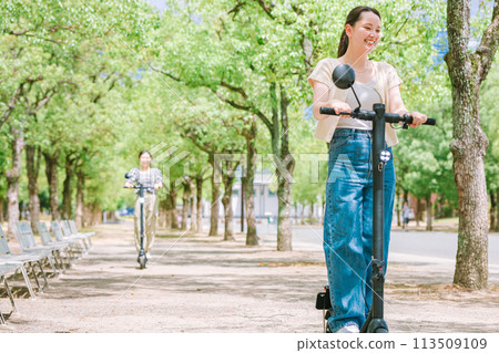A woman riding an electric scooter along a tree-lined street A woman riding an electric scooter along a tree-lined street 113509109