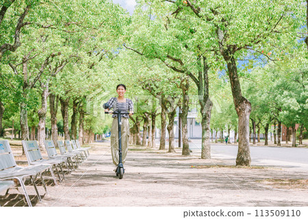 A young woman running on a tree-lined street with an electric kickboard A young woman running on a tree-lined street with an electric kickboard 113509110