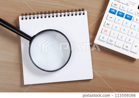 notebook on a brown wooden background with a calculator and magnifying glass 113509166