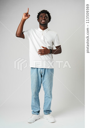 Young African Man in Casual Attire Pointing Upwards With a Smile Against a Grey Background Young African Man in Casual Attire Pointing Upwards With a Smile Against a Grey Background 113509369