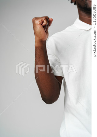 Young African Man in White Shirt Celebrates With Joyful Fist Pump on Grey Background Young African Man in White Shirt Celebrates With Joyful Fist Pump on Grey Background 113509399