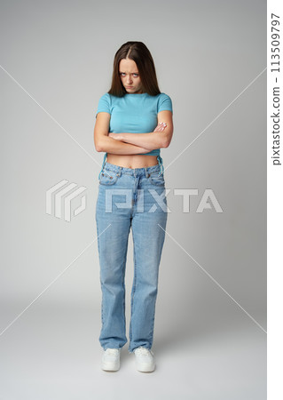Portrait of sad displeased offended young woman in blue T-shirt on gray background Portrait of sad displeased offended young woman in blue T-shirt on gray background 113509797