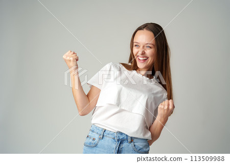 Strong powerful young woman raises arms celebrating success on gray background Strong powerful young woman raises arms celebrating success on gray background 113509988