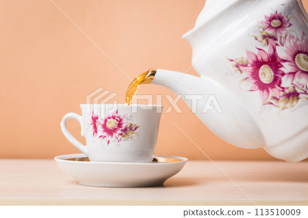 Old-style porcelain kettle pouring tea from jug to cup of tea 113510009