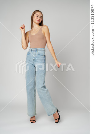 Young Woman Wearing High Rise Jeans and Tank Top posing on gray background in studio Young Woman Wearing High Rise Jeans and Tank Top posing on gray background in studio 113510074