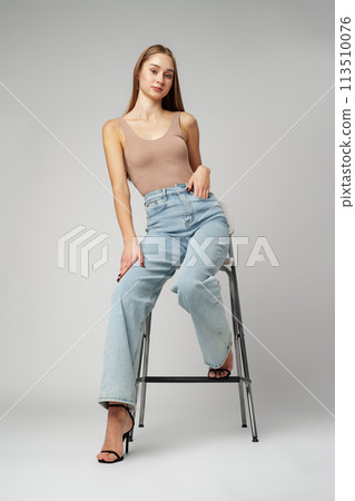 Young Woman Sitting on Stool in High Rise Jeans on gray background Young Woman Sitting on Stool in High Rise Jeans on gray background 113510076