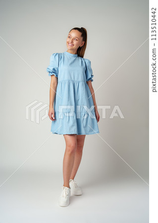 Young happy smiling woman in a light blue dress on a gray background Young happy smiling woman in a light blue dress on a gray background 113510442