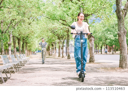 A woman riding an electric scooter along a tree-lined street 113510463