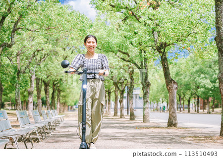 A young woman running on a tree-lined street with an electric kickboard A young woman running on a tree-lined street with an electric kickboard 113510493