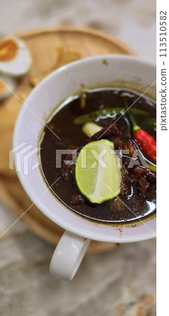 Rawon or Indonesian black beef soup, black color are from indonesian nut called kluwek. Served with lime, chili paste, salted egg, and tempe cracker. Perfect for recipe, article, or any cooking 113510582