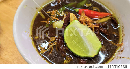 Rawon or Indonesian black beef soup, black color are from indonesian nut called kluwek. Served with lime, chili paste, salted egg, and tempe cracker. Perfect for recipe, article, or any cooking 113510586