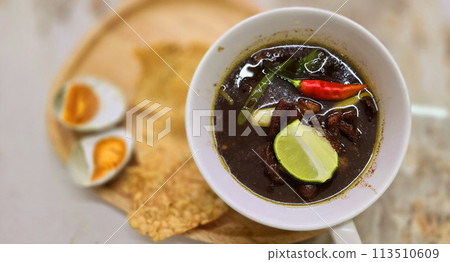 Rawon or Indonesian black beef soup, black color are from indonesian nut called kluwek. Served with lime, chili paste, salted egg, and tempe cracker. Perfect for recipe, article, or any cooking 113510609
