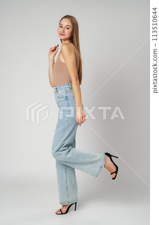 Young Woman Wearing High Rise Jeans and Tank Top posing on gray background in studio 113510644