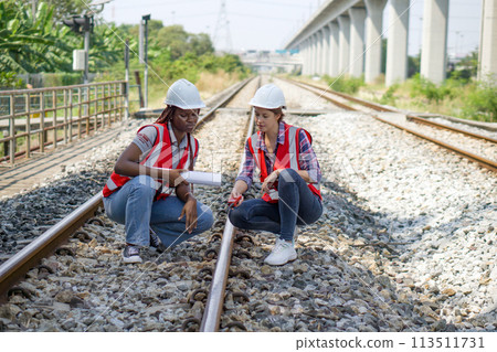 Rail transportation engineer in safety vest and hardhat check the neatness of the railway track while holding walkie-talkie and train route chart. 113511731