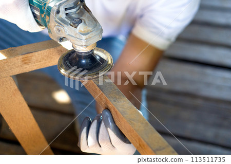 A person works with a power tool, sending sawdust flying as they  shape a piece of wood. A person works with a power tool, sending sawdust flying as they  shape a piece of wood. 113511735