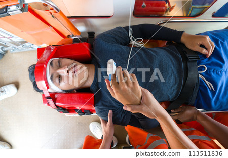 A person is lying on a stretcher with a head immobilizer and is monitored by medical personnel in orange uniform inside an ambulance. Top view 113511836