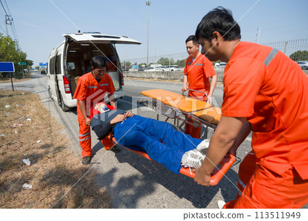 Group of paramedic or emergency medical technician (EMT) in orange uniform helping neck and head accident victim lying on stretcher long spinal board. Urgent assistance during road accident. 113511949