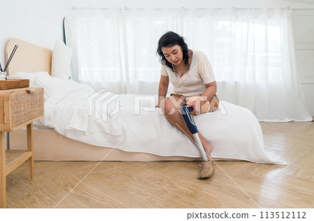 Asian woman disability with prosthetics bionic leg, prosthetic limbs sitting in bedroom at home. 113512112