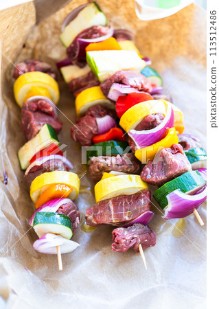 Raw skewers with beef and fresh veggies, wrapped in butcher brown paper, await grilling. Raw skewers with beef and fresh veggies, wrapped in butcher brown paper, await grilling. 113512486