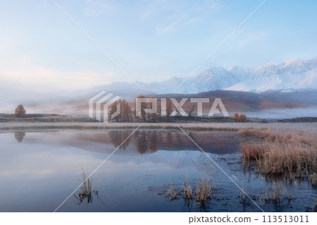 Snowy peaks are reflected in the calm cold water of a mountain l 113513011