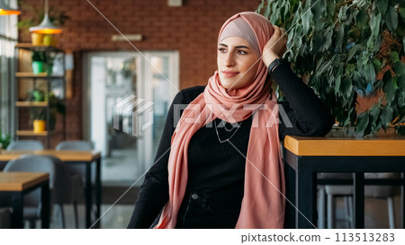 Coffee shop leisure. Cafe rest. Dreamy satisfied woman in hijab enjoying free time spending job break at cozy city coffeehouse. Coffee shop leisure. Cafe rest. Dreamy satisfied woman in hijab enjoying free time spending job break at cozy city coffeehouse. 113513283