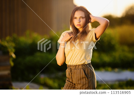 Photo shoot in countryside during golden hour, young European woman posing for photographer outdoors. 113516905