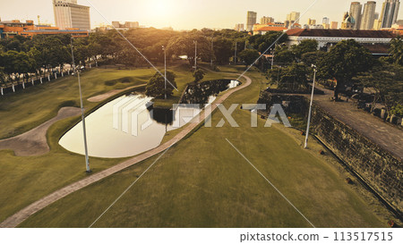 Pond with sun reflection at designed green park aerial. Green grass valey with lake at path 113517515
