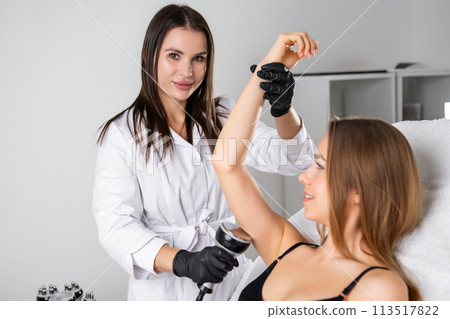 Beautiful young beautician doing ultrasound cavitation on the arm of the young blonde woman. Beautiful young beautician doing ultrasound cavitation on the arm of the young blonde woman. 113517822