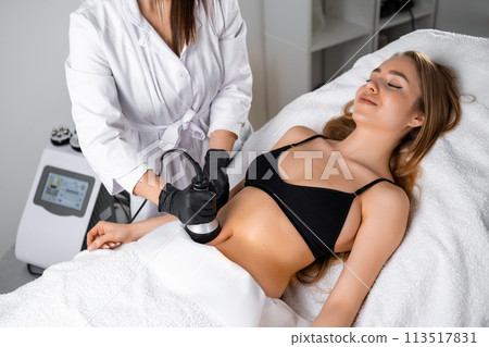 Young woman getting ultrasound cavitation body contouring treatment and anti cellulite therapy. Hardware cosmetology for body sculpting.  113517831