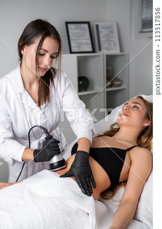 Portrait of young cosmetologist doing a cavitation procedure to young patient. Hardware cosmetologist. Portrait of young cosmetologist doing a cavitation procedure to young patient. Hardware cosmetologist. 113517856