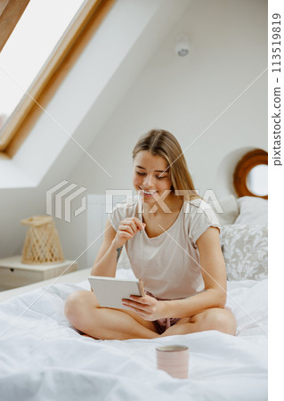 A woman is seated on a wooden bed and making notes in note pad  113519819