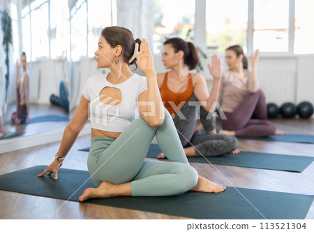 Young woman maintaining mental and physical health attending group yoga class at studio, practicing twisting poses 113521304