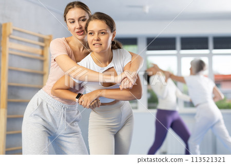 Woman and girl in gym perform basic elements of krav maga self-defense system. Woman and girl in gym perform basic elements of krav maga self-defense system. 113521321