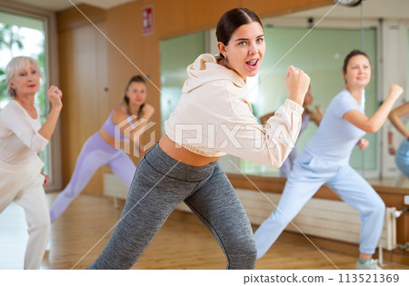 Happy flexible women of different ages exercising active dance with sliding leg to side in fitness center 113521369