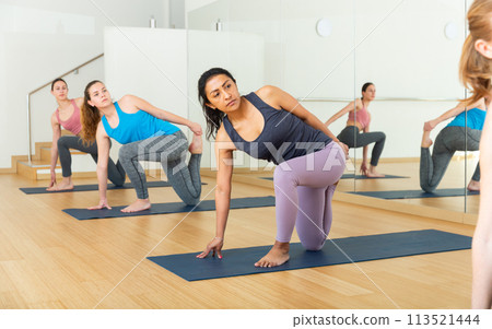 Hispanic woman doing stretching workout during group training 113521444