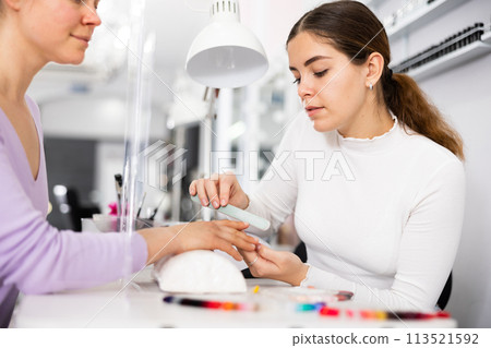 Manicurist files the nails of a young female client 113521592