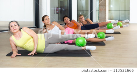 Women practicing pilates with balls at group class in yoga studio Women practicing pilates with balls at group class in yoga studio 113521666
