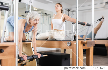 Aged woman exercising on wunda chair in pilates studio Aged woman exercising on wunda chair in pilates studio 113521678