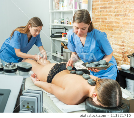 Two masseuses massage the legs and perform a stone therapy procedure 113521710