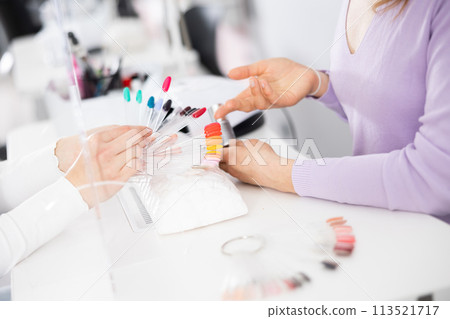 Manicurist helping woman client to choose color of nail polish on palette 113521717