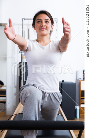 Young Latina practicing pilates on reformer at gym Young Latina practicing pilates on reformer at gym 113521853